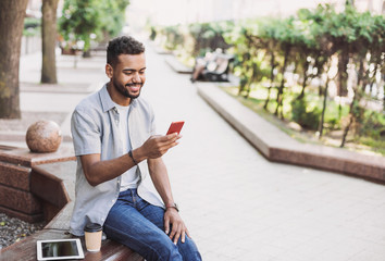 Obraz premium Young handsome business man using smartphone in a city. Cheerful men holding mobile phone. Travel, business, technology concept