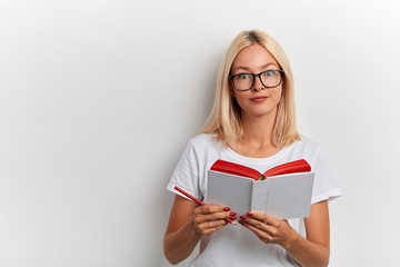 blonde cute clever woman holds notebook and pencil has thoughtful expression, wears stylish glasses, isolated over white background. copy space. education concept. job, profession, occupation