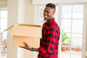 Obraz na płótnie Canvas Young african american man holding a carton box, packing cardboard delivery package at home