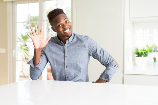 Handsome african american man on white table showing and pointing up with fingers number five while smiling confident and happy.