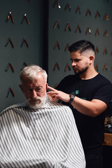 young man trimming old man's hair above ears. close up photo.
