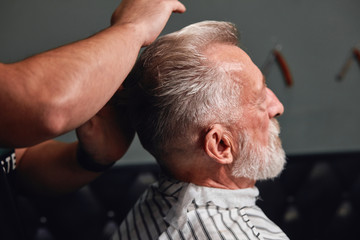 Obraz premium cool hairstyle for real men,stylist combing his client's hair with fantastic neatness. close up side view photo. profile of old man