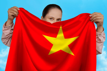 young girl holding in both hands a colored national flag on beautiful shiny silk against a blue sky, state concept, travel, immigration, horizontal, close-up, copy space