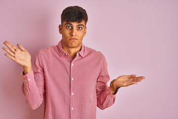 Young indian man wearing elegant shirt standing over isolated pink background clueless and confused...