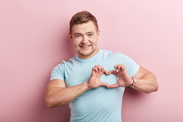 happy strong muscular man wearing casual blue t-shirt over isolated pink background smiling in love showing heart symbol and shape with hands. Romantic concept.I love you.body language