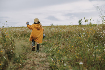 Little girl in raincoat is walking on field