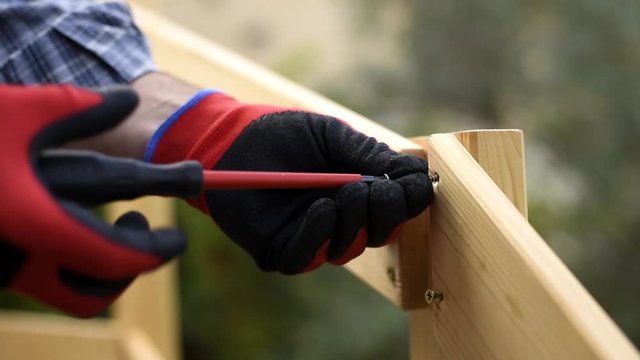 Adult carpenter craftsman with screwdriver screw the screw to fix the boards of a wooden fence. Housework, do it yourself. Footage.