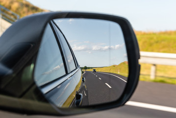 Asphalt road with vehicle reflected in car mirror. Concept of safe driving.