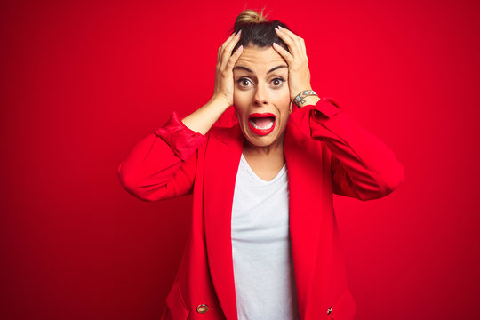 Young beautiful business woman standing over red isolated background Crazy and scared with hands on head, afraid and surprised of shock with open mouth