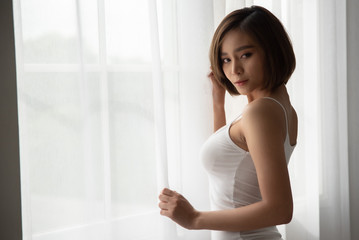 Attractive sexy asian woman standing near balcony window. - obrazy, fototapety, plakaty