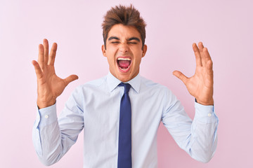 Young handsome businessman wearing shirt and tie standing over isolated pink background celebrating mad and crazy for success with arms raised and closed eyes screaming excited. Winner concept