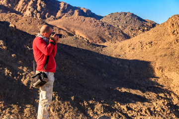 Fototapeta premium Young man taking a photos of mountain range Red Sea Hills in Arabian desert, Egypt