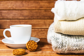 Obraz na płótnie Canvas Stack of cozy knitted warm sweater , wooden background . Sweaters in retro Style and a Cup of hot drink. The concept of warmth and comfort.