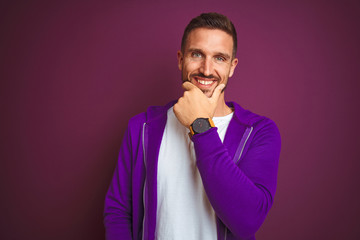 Fototapeta premium Young fitness man wearing casual sports sweatshirt over purple isolated background looking confident at the camera smiling with crossed arms and hand raised on chin. Thinking positive.