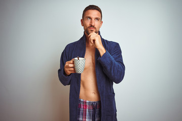 Shirtless man wearing comfortable pajamas and robe drinking cup of coffee serious face thinking about question, very confused idea