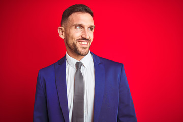 Young handsome business man over red isolated background looking away to side with smile on face, natural expression. Laughing confident.