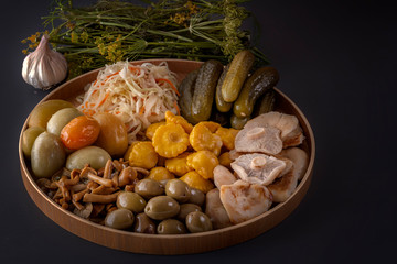 Fermented foods cabbage, peppers, pickles, tomatoes, mushrooms, zucchini, garlic in a large wooden dish on a dark table with spices for salting. Low key.