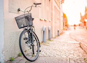 Black bicycle with shopping basket stand near the wall on the street, sunlight on the background, horizontal