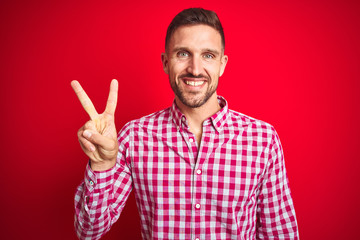 Naklejka premium Young handsome man over red isolated background showing and pointing up with fingers number two while smiling confident and happy.