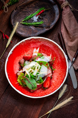 Warm salad of beef tenderloin, arugula, spinach, strawberries and Parmesan in a red plate on a wooden background. Italian cuisine rustic style