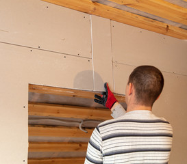 A worker fastens a sheet of drywall to the wall