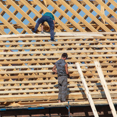 Workers are building the roof of the house from wood