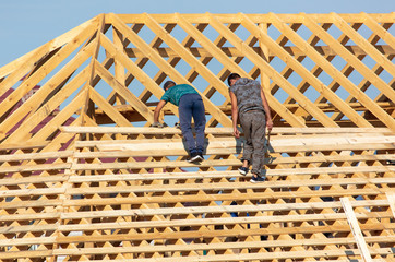 Workers are building the roof of the house from wood