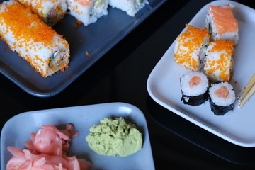 Sushi roll with seafood and soy sauce, wasabi and ginger. Sushi roll with salmon and flying fish caviar on a black table
