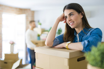 Young couple moving to a new home, beautiful woman smiling leaning on cardboard boxes