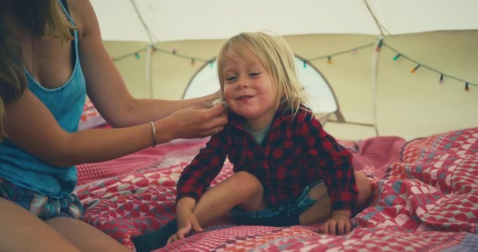 Young mother wiping her toddler's face in a tent
