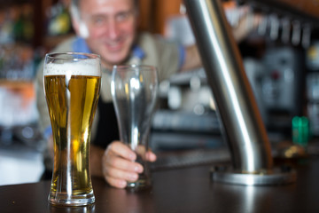 glass of beer on bar counter against background of friendly bartender