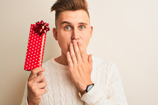 Young handsome man holding valentine gift standing over isolated white background cover mouth with hand shocked with shame for mistake, expression of fear, scared in silence, secret concept