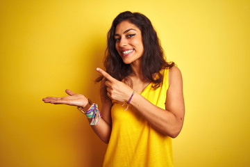 Young beautiful woman wearing t-shirt standing over isolated yellow background amazed and smiling to the camera while presenting with hand and pointing with finger.