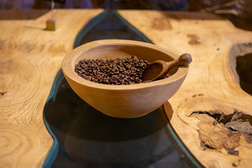 Table made of wood and glass. Coffee beans and spoon are in a wooden bowl.