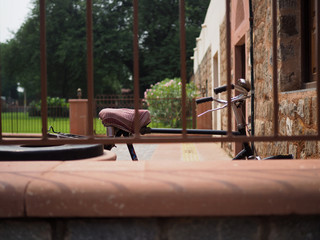 Closeup of old rusty bicycle with red seat parking outside with old metal fence in the foreground. Selected focus.