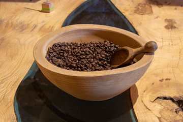 Table made of wood and glass. Coffee beans and spoon are in a wooden bowl.