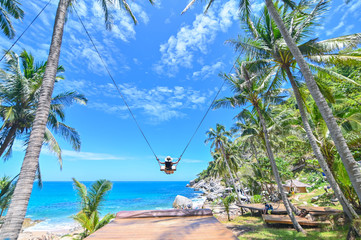 A young girl swinging on a swing between trees on the beach of a tropical island.nd enjoy the...