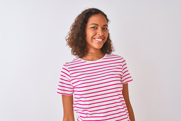 Young brazilian woman wearing pink striped t-shirt standing over isolated white background looking away to side with smile on face, natural expression. Laughing confident.