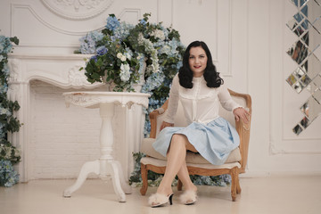 Pin up cute good girl at a retro white apartment near the table. Pretty vintage woman in stockings in stylish room with flowers alone.