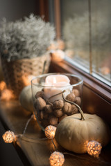 autumn cosy pumpkin, candles and autumn plants on window with led lights bokeh