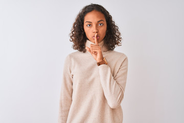 Young brazilian woman wearing turtleneck sweater standing over isolated white background asking to be quiet with finger on lips. Silence and secret concept.