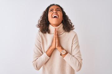 Young brazilian woman wearing turtleneck sweater standing over isolated white background begging...