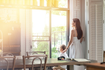 Portrait of young woman and 4-year-old boy in white room. Mother and toddler are standing near the window indoors. Mom and son concept. Horizontal shot