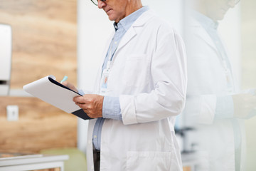 Side view mid section portrait of unrecognizable senior doctor holding clipboard and taking notes while standing in modern office, copy space - Powered by Adobe