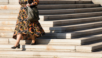 Legs of a mature plus size woman walking down city stairs in  long black and orange dress