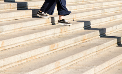 Legs of young woman iin sneaker shoes walking down city stairs