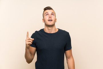 Young handsome blonde man over isolated background pointing up and surprised