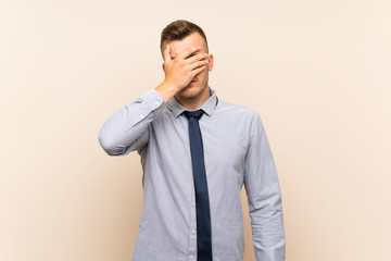 Young blonde businessman over isolated background covering eyes by hands