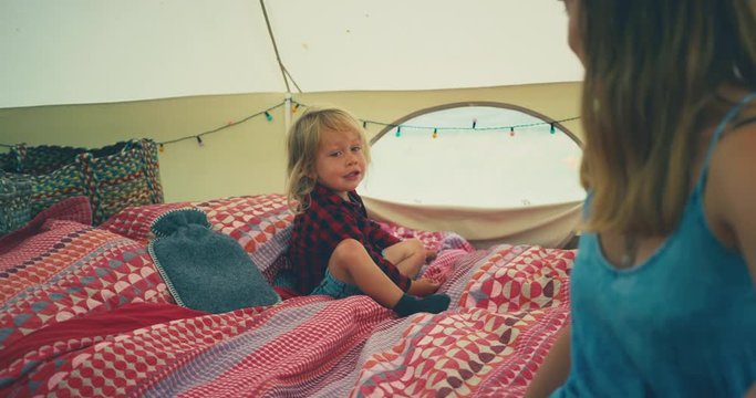 Mother and toddler sitting on bedding in a large tent