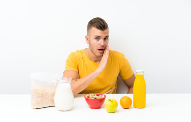 Young blonde man having breakfast whispering something